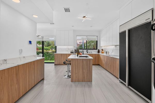 Renovated kitchen with walnut-tone lower cabinets, white uppers, a center island and a black panel refrigerator