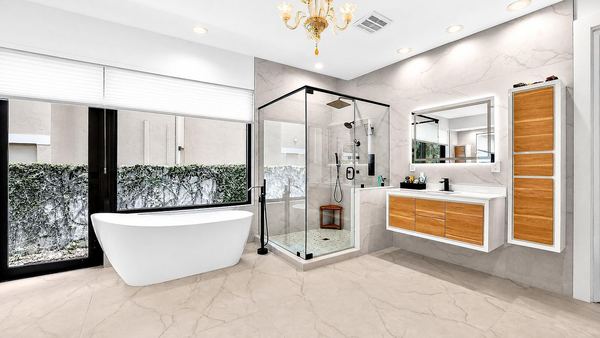 Wide view of the primary bath: soaking tub, glass shower, floating vanity and chandelier