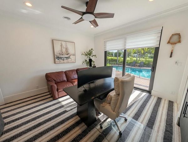 Study with a striped rug, a leather sofa and a window looking out to the pool